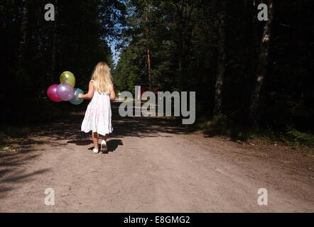 Fille marchant sur la route transportant un tas de ballons, Suède Banque D'Images
