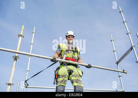 Low angle portrait of smiling construction worker holding baguette métallique contre le ciel Banque D'Images