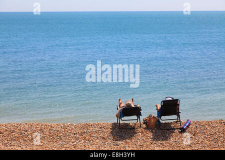 Deux personnes dans des chaises longues sur la plage de galets par mer de l'arrière. Banque D'Images