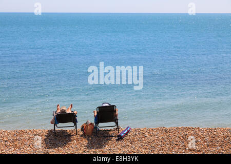 Deux personnes dans des chaises longues sur la plage de galets par mer de l'arrière. Banque D'Images