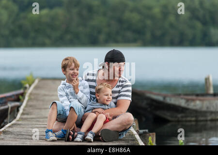 Allemagne, Rhénanie-Palatinat, Laacher See, père assis avec deux fils on jetty Banque D'Images