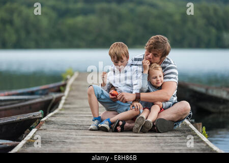 Allemagne, Rhénanie-Palatinat, Laacher See, père assis avec deux fils on jetty Banque D'Images
