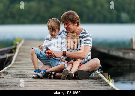 Allemagne, Rhénanie-Palatinat, Laacher See, père assis avec deux fils on jetty Banque D'Images