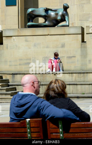 Leeds, UK. Les gens se détendre au soleil à côté de l'Henry Moore sculpture 'Femme' inclinables à l'extérieur de la galerie d'Art de Leeds. Banque D'Images