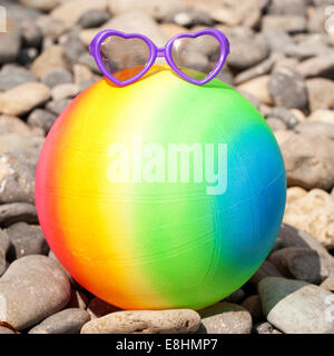 Vacances d'concept. Ballon de plage de couleur arc-en-ciel avec des lunettes de soleil sur les cailloux, prêt pour votre texte ou des symboles. Banque D'Images