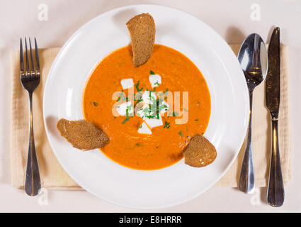 Soupe de butternut ou courge délicieuse avec du fromage, des biscottes et des herbes fraîches, vue de dessus dans un bol blanc avec couverts alongsi Banque D'Images