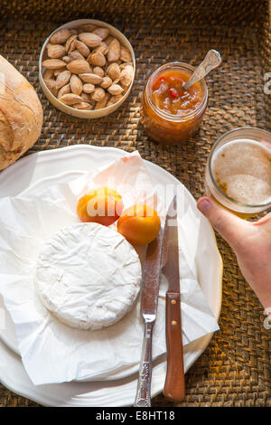 Le camembert, abricots, chutney d'abricots, amandes, main tenant la bière, situé sur le plateau tissé Banque D'Images