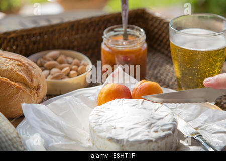 Le camembert étant coupé, avec l'abricot, abricot, amandes chutney et de la bière, situé sur le plateau tissé Banque D'Images