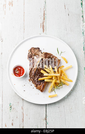 T-bone steak avec frites salées sur plaque blanche sur fond de bois bleu Banque D'Images