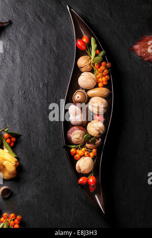 Plaque en céramique décorative avec des noix, des baies et des champignons sur fond noir. Banque D'Images