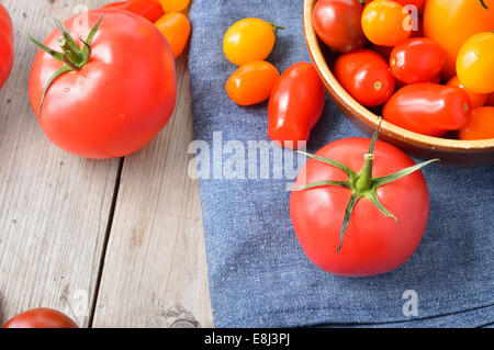 Différents types colorés des tomates dans un bol sur la table en bois. Rouge, jaune, grandes et petites tomates. Copier l'espace. Banque D'Images