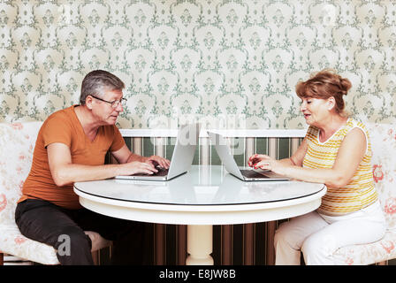 Middle-aged couple assis en face de l'autre moyen d'ordinateurs portables Banque D'Images