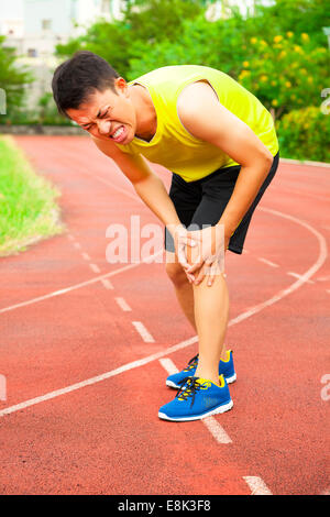 Young male runner souffrant de blessures du genou sur la piste dans le stade Banque D'Images