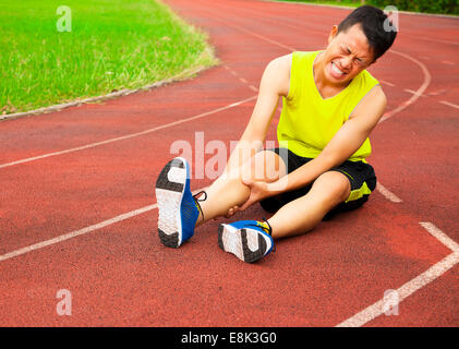 Young male runner souffrant de crampes de jambe sur la piste dans le stade Banque D'Images