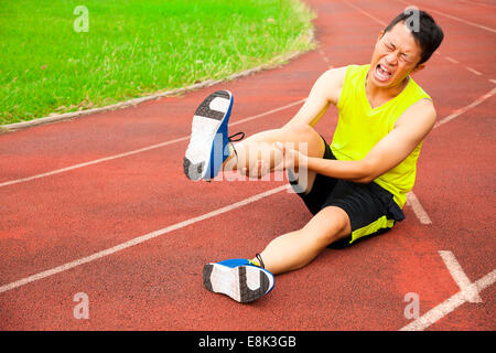 Young male runner souffrant de crampes de jambe sur la piste dans le stade Banque D'Images