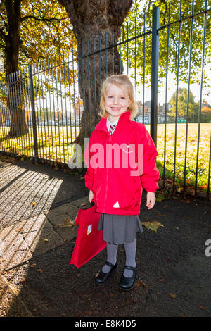 Un enfant de 4 ans / fille dans son nouvel uniforme rouge aller à / sur le chemin de sa classe d'accueil à l'enfant de l'État l'école primaire. UK. Banque D'Images