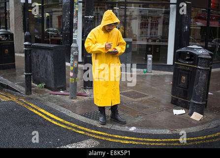 Un homme portant un manteau imperméable jaune donne des dépliants sur Brick Lane dans l'Est de Londres, au Royaume-Uni. Banque D'Images