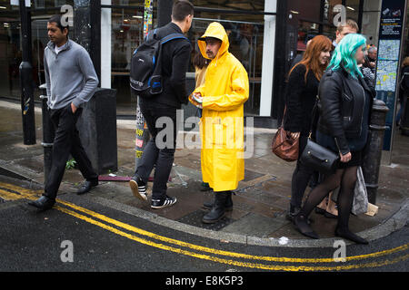 Un homme portant un manteau imperméable jaune donne des dépliants sur Brick Lane dans l'Est de Londres, au Royaume-Uni. Banque D'Images