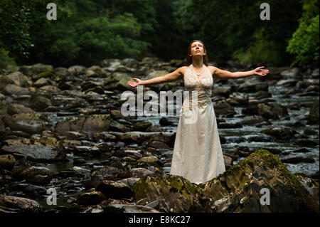 Corbeille la robe : un 'bride' de porter sa robe de mariage debout dans une rivière avec ses bras tendus l'adoration de la nature