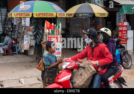 Petits enfants cambodgiens mendicité harceler les femmes sur moto en face de shop le long de la route dans le Delta du Mékong du Vietnam. Banque D'Images