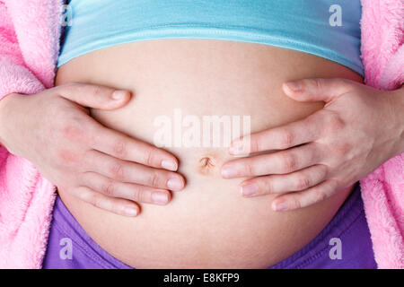 Femme enceinte se tenant la main sur son ventre en portant des vêtements colorés, studio shot on white background Banque D'Images