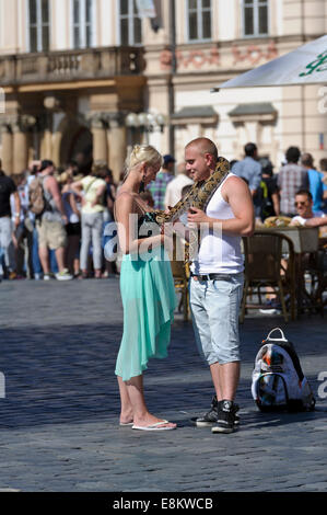 Un jeune couple standing in e milieu de la place de la vieille ville avec un gros serpent sur les épaules de l'homme, Prague, République tchèque. Banque D'Images