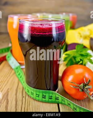 Le jus de betterave dans l'avant-plan et le jus de carotte, citrouille, concombre et tomate dans un grand verre, légumes sur fond de wo Banque D'Images