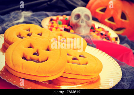 Une pile de cookies en forme de citrouille et quelques bonbons Halloween effrayant avec différents ornements dans l'arrière-plan, comme un crâne, c Banque D'Images