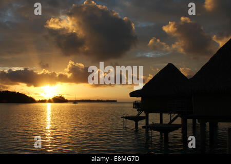 Bungalows sur pilotis au lever du soleil dans une lagune tropicale Banque D'Images