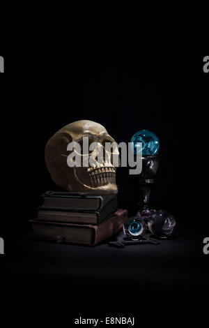 Crâne humain d'ombre sombre et reposant sur de vieux livres dans un pool de lumière. Crystal Ball est allumé en bleu. Banque D'Images