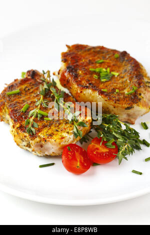 Rôti de porc frais sur grill steak on white plate servant avec les tomates cerise et d'herbes. Sur fond blanc, selective focus Banque D'Images