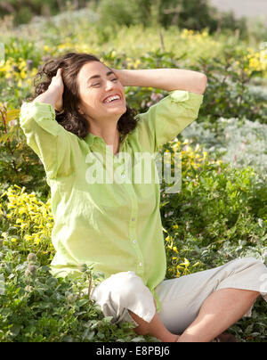 Portrait de femme assise dans l'herbe sauvage, rire Banque D'Images