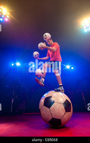 Zhora Oganisyan, le jongleur de football du cirque d'Etat de Moscou, les tentatives d'équilibre sur un géant tout en jonglant avec des ballons de football 3 avec sa main en même temps et d'essayer de "suivre" une pichenette par football supplémentaires d'un pied sur l'autre, à l'Alexandra Palace comprend : Zhora Oganisyan Où : London, Royaume-Uni Quand : 10 Avr 2014 Banque D'Images