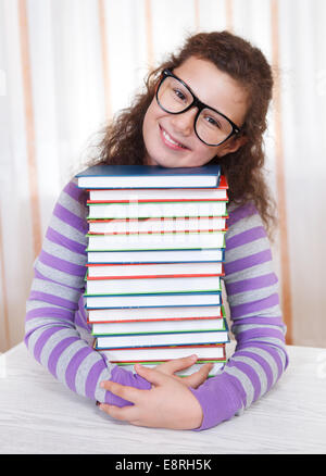 Petite brunette smiling girl avec piles de livres Banque D'Images