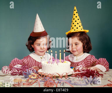 1960 TWIN GIRLS WEARING PARTY HATS ET gâteau d'ANNIVERSAIRE AVEC CINQ BOUGIES Banque D'Images