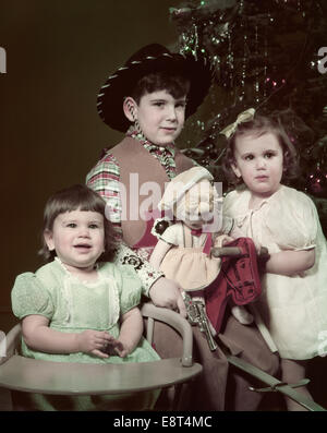 Années 1940 Années 1950 TROIS ENFANTS EN ARBRE DE NOËL Garçon Fille COSTUME Chapeau de cow-boy à la poupée TODDLER IN CHAIR Banque D'Images