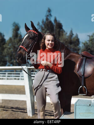 Années 1940 Années 1950 SMILING TEEN GIRL WEARING JODHPURS RIDING HORSE BY FENCE Banque D'Images