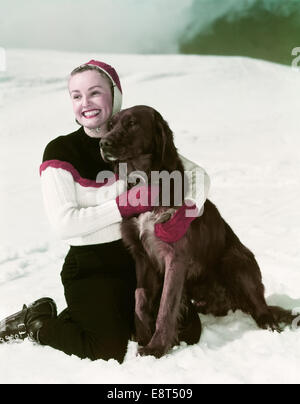 1940 SMILING WOMAN WEARING SKI OUTFIT À GENOUX EN SERRANT LA NEIGE chien Setter Irlandais Banque D'Images