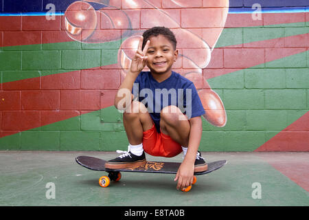 African American boy sitting on skateboard par murale urbaine Banque D'Images