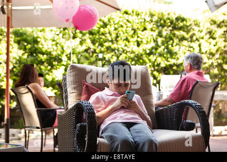 Bored boy using cell phone at party Banque D'Images