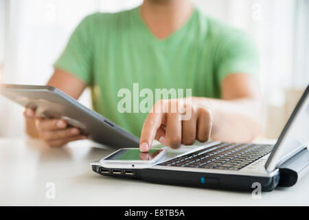 Mixed Race man using cell phone, ordinateur portable et tablette numérique Banque D'Images