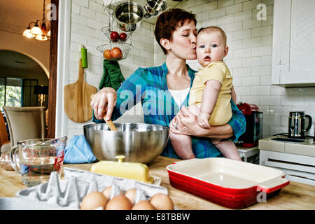 Mère embrassant bébé caucasien et la cuisson dans la cuisine Banque D'Images