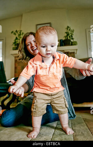 Caucasian mother helping baby marche sur plancher du salon Banque D'Images