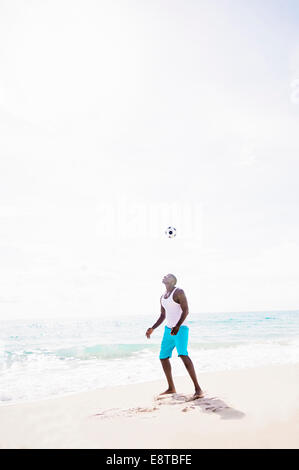 Mixed Race man Playing with soccer ball on beach Banque D'Images