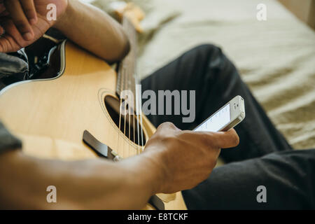 Mixed Race boy avec guitare using cell phone Banque D'Images