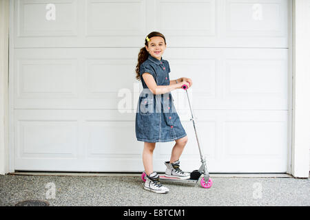 Mixed Race girl smiling on scooter in driveway Banque D'Images