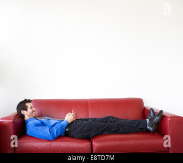 Mixed Race businessman using cell phone on sofa Banque D'Images