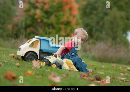 Un deux-année-vieux garçon joue avec des camions de jouets sur une journée d'automne. Banque D'Images