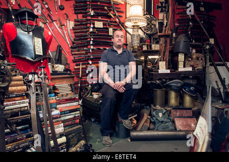 Un commerçant est à sa boutique d'antiquités militaires historiques entouré par des fusils, des sabres, des fusils, des armures, etc. Banque D'Images