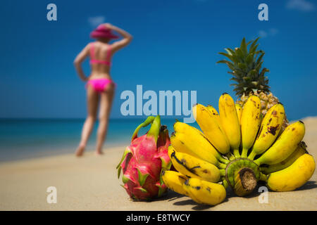 Les fruits tropicaux et d'une femme en bikini en train de bronzer sur la plage sur fond de mer. Scène idéaliste des voyages d'agrément. Banque D'Images